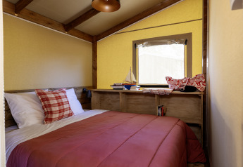 Schlafzimmer in einem Safarizelt mit Holzbalken, Doppelbett, roter Bettdecke und Fenster in La Davière Plage.