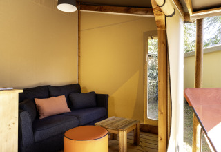 Interior de una tienda safari en Hut Cotton Confort de Flower Camping La Davière Plage, con sofá y mesa.