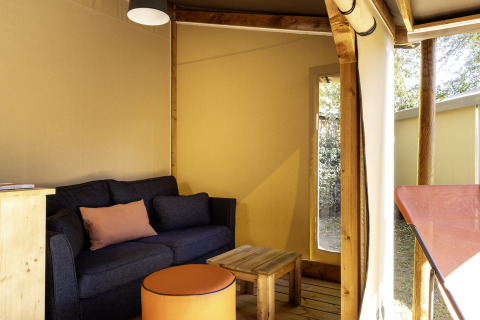 Interior de una tienda safari en Hut Cotton Confort de Flower Camping La Davière Plage, con sofá y mesa.