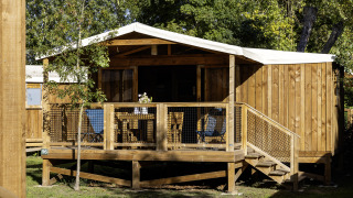 Tenda safari CosyFlower Confort con veranda in legno, sedie e circondata da un ambiente verde.