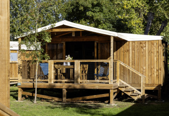 Tenda safari CosyFlower Confort con veranda in legno, sedie e circondata da un ambiente verde.