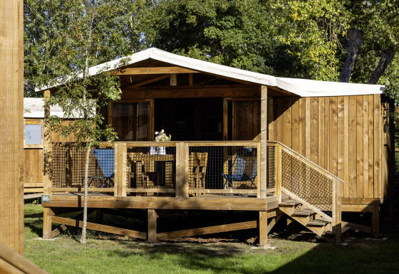 Tenda safari CosyFlower Confort con veranda in legno, sedie e circondata da un ambiente verde.