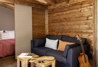 Gezellige leefruimte in een safaritent met houten wanden, donkere zetel, gitaar en zicht op slaapkamer.