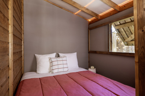 Interno di una tenda safari con letto matrimoniale e pareti in legno al Flower Camping La Davière Plage, Francia.