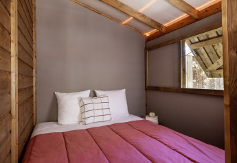 Interno di una tenda safari con letto matrimoniale e pareti in legno al Flower Camping La Davière Plage, Francia.