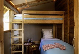 Interior de tienda safari en CosyFlower Confort, Flower Camping La Davière Plage, con litera de madera.