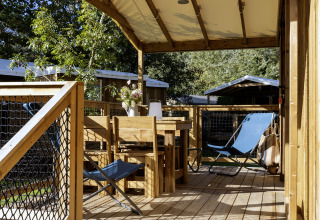 Overdekt houten terras met eetset en blauwe ligstoel aan de CosyFlower Confort safaritent in Frankrijk.
