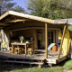 Safari tent Hut Cotton Confort met houten veranda, tuinstoelen, picknicktafel en surfplank in het groen.