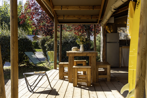 Terraza de madera de la tienda safari Hut Cotton Confort en Flower Camping La Davière Plage, Francia, con bancos.
