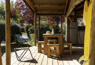 Terraza de madera de la tienda safari Hut Cotton Confort en Flower Camping La Davière Plage, Francia, con bancos.