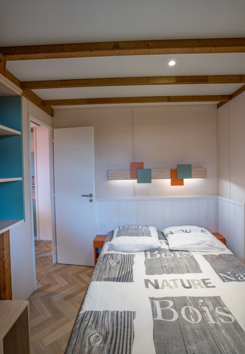 Camera da letto del Cottage Cannelle al Flower Camping La Davière Plage, Francia, con letto matrimoniale e travi.