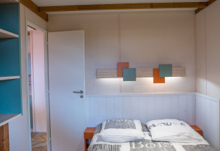 Camera da letto del Cottage Cannelle al Flower Camping La Davière Plage, Francia, con letto matrimoniale e travi.