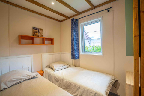 Camera con due letti singoli, finestra e arte Buddha al Cottage Cannelle, Flower Camping La Davière Plage, Francia.
