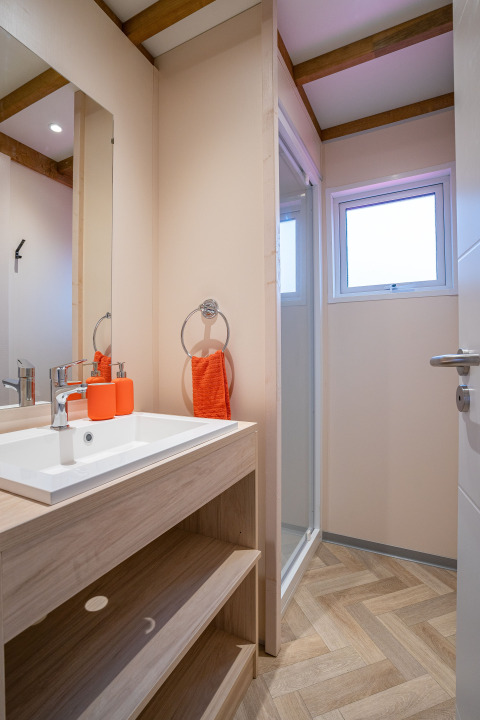 Baño moderno en Cottage Cannelle, Flower Camping La Davière Plage, con lavabo de madera y toques naranjas.