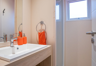 Baño moderno en Cottage Cannelle, Flower Camping La Davière Plage, con lavabo de madera y toques naranjas.