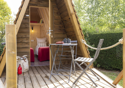 Knusse Cabadienne-hut met houten terras, tafel, stoelen en twee eenpersoonsbedden binnen.