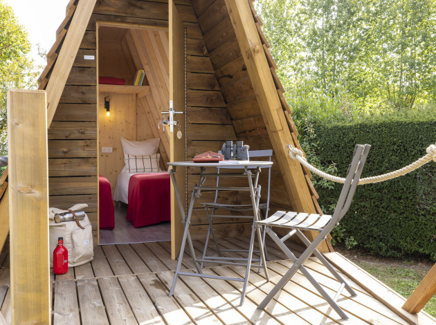 Knusse Cabadienne-hut met houten terras, tafel, stoelen en twee eenpersoonsbedden binnen.