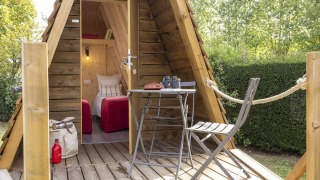 Gemütliche Cabadienne-Hütte aus Holz mit Veranda, Tisch, Stühlen und zwei Betten im Innenraum.