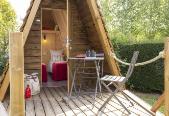 Knusse Cabadienne-hut met houten terras, tafel, stoelen en twee eenpersoonsbedden binnen.