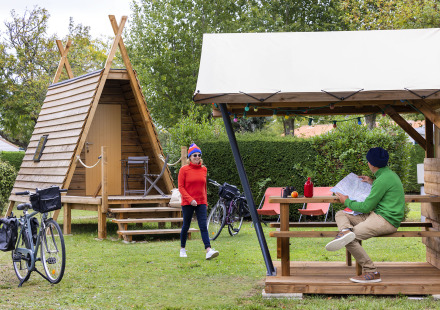 Twee mensen bij een Cabadienne-hut op Flower Camping La Davière Plage in Frankrijk met fietsen en bomen.
