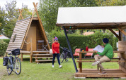 Dos personas junto a una cabaña Cabadienne en Flower Camping La Davière Plage en Francia con bicicletas y árboles.