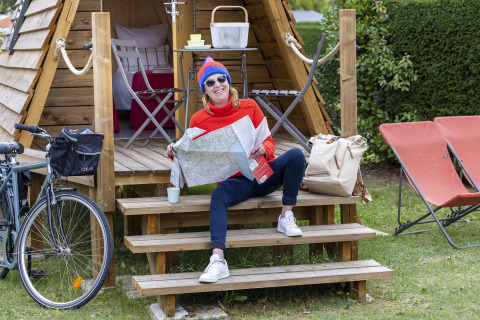 Mujer con mapa sentada en las escaleras de una cabaña Cabadienne en Flower Camping La Davière Plage, Francia.
