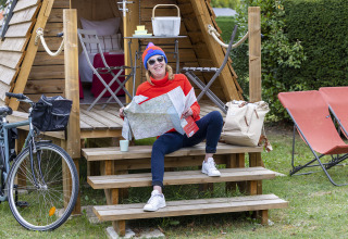 Mujer con mapa sentada en las escaleras de una cabaña Cabadienne en Flower Camping La Davière Plage, Francia.