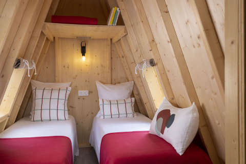 Vista interior de dos camas individuales en una cabaña de madera Cabadienne en Flower Camping La Davière Plage.