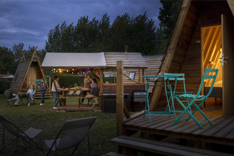 Foto nocturna de personas disfrutando en cabañas Cabadienne en Flower Camping La Davière Plage, Francia.