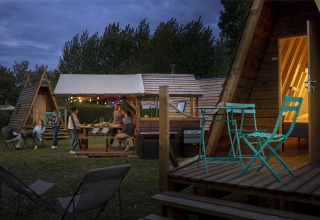 Foto nocturna de personas disfrutando en cabañas Cabadienne en Flower Camping La Davière Plage, Francia.
