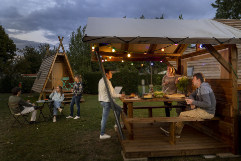 Persone cenano all’aperto sotto un gazebo vicino a una cabina Cabadienne, Flower Camping La Davière Plage, Francia.