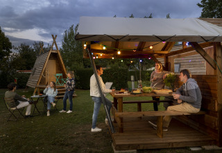 Groep mensen eet samen in de buitenlucht bij een Cabadienne-hut op Flower Camping La Davière Plage in Frankrijk.