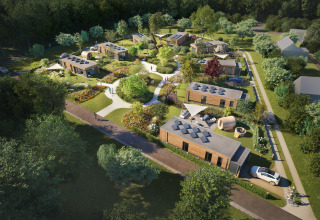 Vue aérienne d’un lodge moderne avec cabanes en bois, chemins paysagés, jardins et forêt environnante.