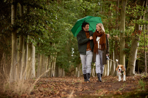 Una coppia passeggia con il cane sotto un ombrello verde su un sentiero nel bosco vicino a un lodge.