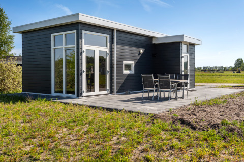 Modernes Turfsteker Chalet bei De Tien Heugten, Niederlande, mit schwarzer Fassade und Terrassentisch.