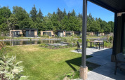 Blick auf die Batenburgh Deluxe Lodge im Veluwepark de Bosgraaf, Niederlande, mit Teich und moderner Terrasse.