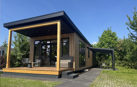 Moderne Sunlodge med træbeklædning, overdækket terrasse og udendørs siddepladser under blå himmel.