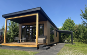 Moderne Sunlodge mit Holzverkleidung, überdachter Terrasse und Garten unter klarem, blauem Himmel.