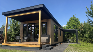 Sunlodge moderna con fachada de madera, porche cubierto y muebles de exterior bajo un cielo azul claro.