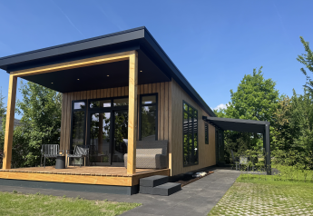 Sunlodge moderna con fachada de madera, porche cubierto y muebles de exterior bajo un cielo azul claro.