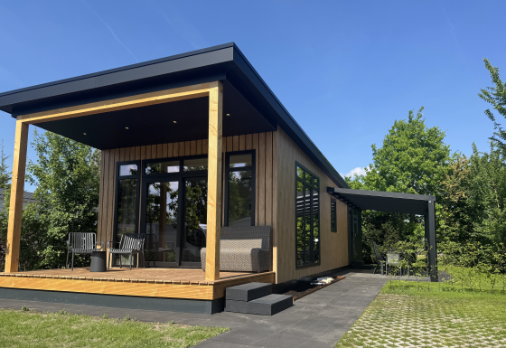 Moderne Sunlodge met houtbekleding en overdekt terras met zitplaatsen onder een stralend blauwe lucht.