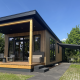 Moderne Sunlodge med træbeklædning, overdækket terrasse og udendørs siddepladser under blå himmel.