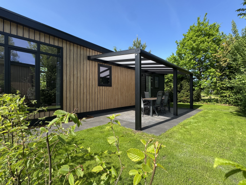 Moderne hytte med træfacade og overdækket terrasse ved Holiday Park 't Rheezerwold i Holland, omgivet af grønne planter.