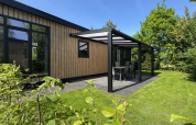 Moderne Sunlodge met houten gevel en overdekt terras bij Holiday Park 't Rheezerwold, omgeven door groen.