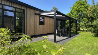 Moderne Sunlodge met houten gevel en overdekt terras bij Holiday Park 't Rheezerwold, omgeven door groen.