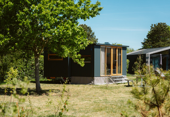 Moderne tiny house Klapkot C20 in een groene omgeving met bomen en een heldere blauwe lucht.
