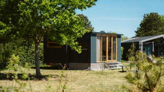 Moderne tiny house Klapkot C20 tussen bomen en groen met een heldere blauwe lucht op de achtergrond.
