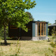 Moderne tiny house Klapkot C20 i grønne omgivelser med træer og blåt himmel i baggrunden.