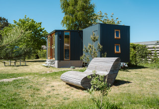 Klapkot C20 tiny house in vakantiedomein De Klepperstee, Nederland, met houten ligzetel in de tuin.