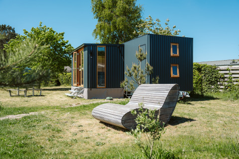 Tiny house Klapkot C20 bij vakantiepark De Klepperstee in Nederland, met houten ligstoel op het grasveld.